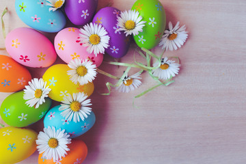 Wall Mural - Close up and top view of colorful painted easter eggs decoration with fresh white blooming daisies on wooden background. Happy Easter background