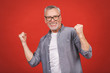 © denis_vermenko - Happy mature senior man in casual using smartphone and making winner gesture isolated over red background.