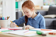 © Seventyfour - Portrait of red haired teenage girl drawing pictures sitting at table at home and smiling, copy space