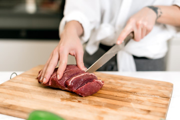 Brunette woman cooking and eating red meat steak with glass of red wine. Housewife concept