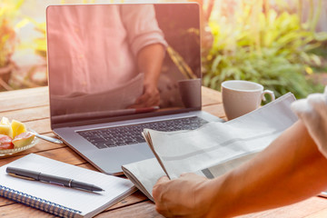 Businessman reading newspaper with pen and notebook and laptop on table.