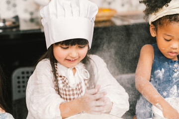 Cute mixed race and African American kid girls baking or cooking together in home kitchen. Education activity, youth culture, or smart young children concept