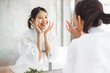 © Nattakorn - Asian woman cleaning face front of mirror, skin care and cosmetic removal concept