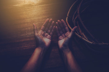 close up of woman hands prays near vine with thorns made like the crown of thorns of Jesus on wooden background  with light from above. Christian concept , Easter concept, copy space, vintage tone.