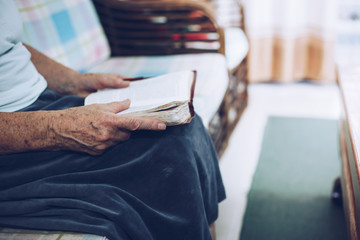 Adult Christian woman hold and reading bible on sofa at home. Christian concept background with copy space. 