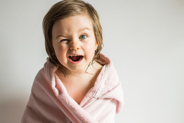 Funny Emotional Toddler Baby Girl Wrapped in a Towel After Shower or Bath on Neutral Background