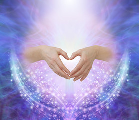 Wall Mural - Healers hands making a humble heart shape - female hands forming a heart shape against a pink circle surrounded by ethereal blue and beautiful glittering sparkles with copy space above