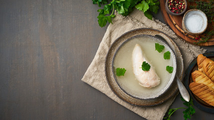 Wall Mural - Chicken broth with chicken fillet, parsley and toast on dark brown background, top view, copy space