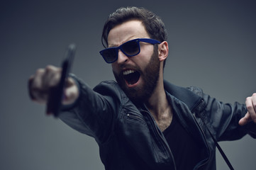 Frontal portrait of a serious bearded brutal man in sunglasses and leather jacket, shows the gesture clenched fist, isolated on a dark grey background. Confident style.