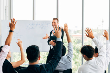 Many business people participants raising up their hand in business seminar conference event inside corporate company office with speaker in front