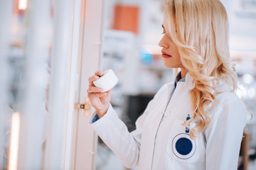 Wall Mural - Portrait of a blonde female pharmacist taking creme from aisle in drugstore.