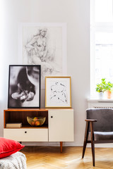 Grey retro armchair next to withe wooden cabinet with golden bowl and posters