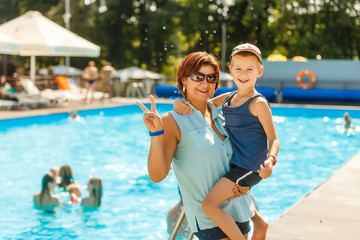 Close-up portrait of beautiful mother with her son standing swimming pool and laughing during vacation on warm summer day