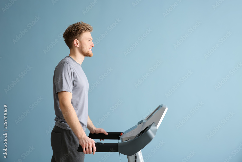Sporty young man training on treadmill against color background