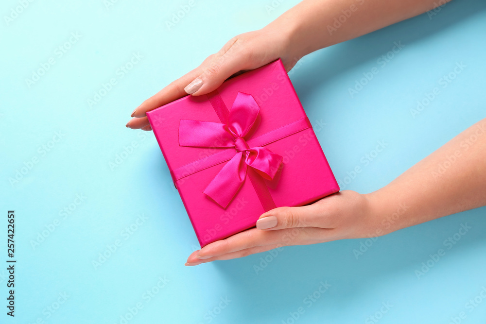 Female hands with gift box on color background