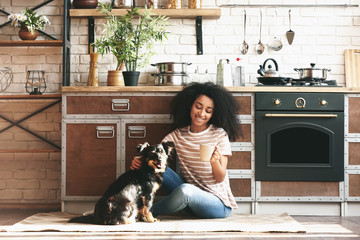 Wall Mural - African-American woman with cute funny dog drinking coffee in kitchen