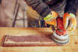 © astrosystem - Male carpenter using orbital electric sander in a retro vintage workshop.