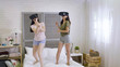 © PRPicturesProduction - Group of asian female friends experiencing virtual reality headset playing tennis match game standing jumping on bed. girls wearing vr goggles having fun together. young people technology concept.