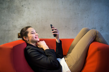 Wall Mural - A young businesswoman with smartphone sitting on red armchair in office.