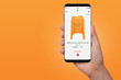 Female hand buying yellow hoodie online on her phone, isolated on orange background