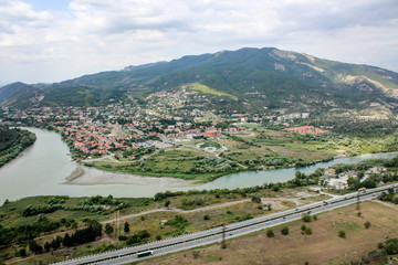 The merger of two rivers into one. The ancient capital of Georgia - city Mtskheta. Hilly terrain, mountains. Houses with red roofs, road, church. View from the lookout monastery Jvari, Georgia. Summer