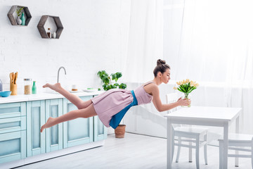 Wall Mural - young elegant barefoot woman levitating in air with tulips