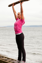 A Young, Healthy Woman Uses Found Driftwood And A Narrow Bulkhead To Exercise On A Rustic Beach.