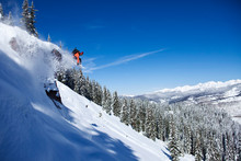 A Athletic Snowboarder Jumping Off A Cliff On A Sunny Powder Day In Vail, Colorado.