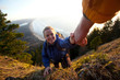 © Cavan Images - One person helping another up steep section of trail while hiking