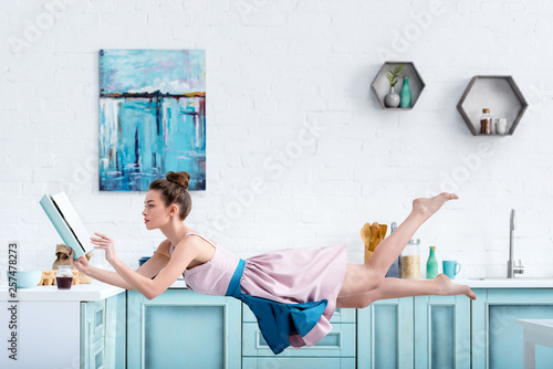 Cuadros en Lienzo young concentrated barefoot woman levitating in air while reading recipe in cook
