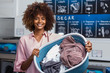 © Samuel B. - Young black African American woman holding a basket of clothes to be washed in a automatic laundry