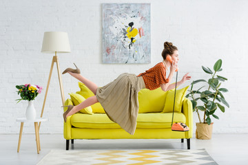 Wall Mural - side view of elegant young woman levitating in air and talking on vintage telephone in living room