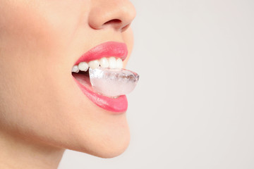 Sticker - Young woman holding ice cube in mouth on light background, closeup. Space for text