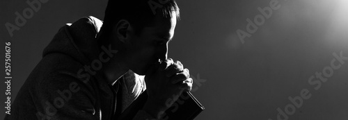 Fotomural Religious young man praying to God on dark background, black and white effect