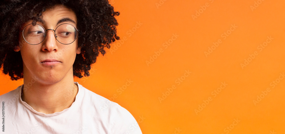 Black millennial man looking skeptically aside at empty space - obrazy, fototapety, plakaty 