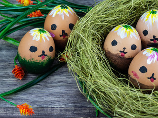 eggs with painted faces in a straw nest on a wooden background