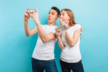 Young excited couple standing , playing games on mobile phones, on a blue background