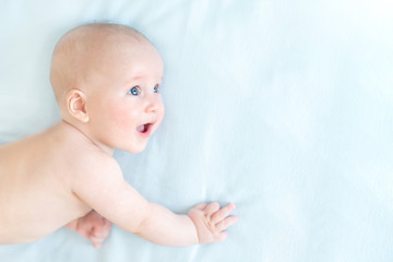 Profile portrait of cute little baby boy lying on blue blanket and looking aside. Child with open mouth and wide opened eyes. Astonished surprised kid. Copyspace