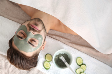 Wall Mural - Young man with clay mask on his face in spa salon, above view