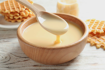 Spoon of pouring condensed milk over bowl on table, closeup. Dairy products