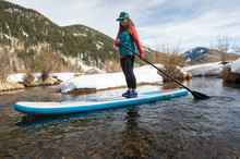 Woman Paddle Boarding In River In Winter, Aspen, Colorado, USA