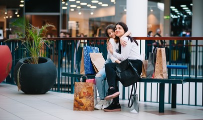 Wall Mural - Beautiful young mom and teenage daughter are holding shopping bags and smiling while doing shopping in mall. Family shopping.