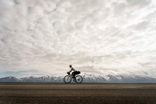 A Cyclist Riding Along A Road Against Snowcapped Mountains