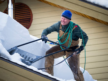 Man Clears Snow Off Of Roof In Winter With Shovel And Saw