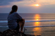 © Cavan Images - Woman sitting on rock at the beach and looking sunset view