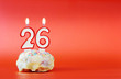 Twenty six years birthday. Cupcake with white burning candle in the form of number 26. Vivid red background with copy space