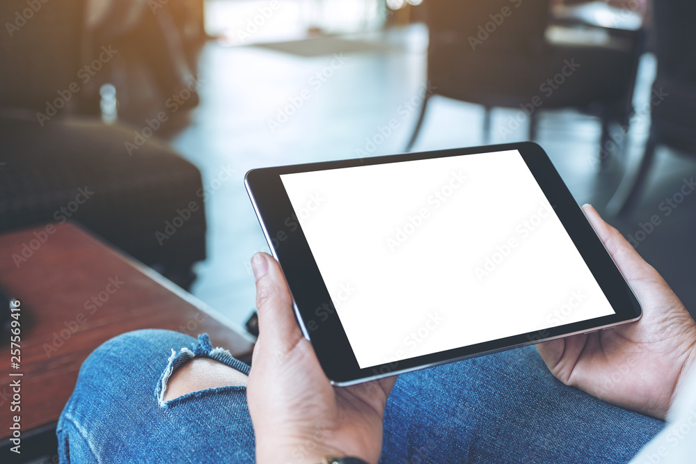 Mockup image of a woman sitting and holding black tablet pc with blank white desktop screen horizontally in cafe - obrazy, fototapety, plakaty 