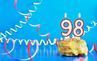 Birthday of ninety eight years. Cupcake with white burning candle in the form of number 98. Vivid blue background with copy space