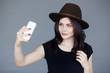 © Dragosh - A cute brunette girl in brown hat,green eyes and wavy hair makes her selfie and smiles sweetly at gray background.Horizontal view.