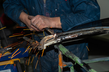 Wall Mural - Close-up view strong man is a welder in working overalls without gloves on arms, a metal product is welded with a welding machine in the garage workshop, blue smoke and orange sparks fly to the sides